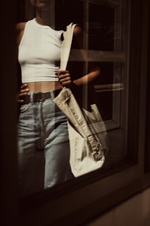 A casual street scene featuring a model in a crisp white shirt and high-waisted jeans, holding a leather tote.