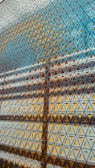 Geometric patterns formed by a series of triangular motifs create a grid-like structure. The interplay of light and shadow adds depth and complexity to the repetitive design, with vibrant shades of yellow and cool tones of blue dominating the color palette.