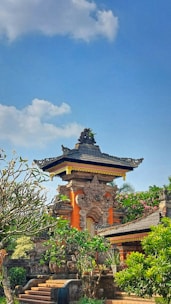 Ancient temple gates framed by vibrant tropical flowers under a bright blue sky.