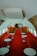 The interior of a vintage airplane features a long aisle lined with plush red seating on both sides. Each seat section includes white round tables in front of the seating areas. The design is reminiscent of mid-20th century luxury, with a spacious cabin and minimalist decor.