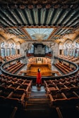 A wide shot of the concert hall bathed in red and white tones, capturing the cultural ambiance.