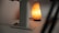 A warm, glowing salt lamp sits on a flat surface, casting a soft, ambient light. It's next to a metallic structure, likely a part of a stand or table, partially visible in the foreground.