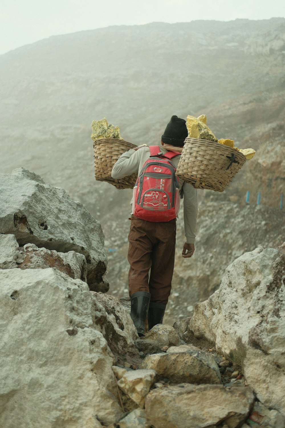 a man with two baskets walking up a mountain