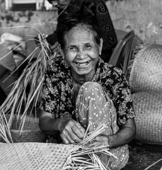 A smiling rural woman carefully weaving colorful threads into a vibrant handmade basket.