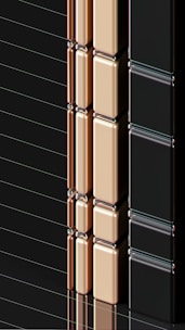 A series of glossy, rectangular tiles arranged vertically with a metallic finish. The tiles are colored in gold, copper, and black, creating a sleek and modern appearance. The surface reflects light, highlighting the smooth texture and polished edges.