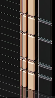 A series of glossy, rectangular tiles arranged vertically with a metallic finish. The tiles are colored in gold, copper, and black, creating a sleek and modern appearance. The surface reflects light, highlighting the smooth texture and polished edges.