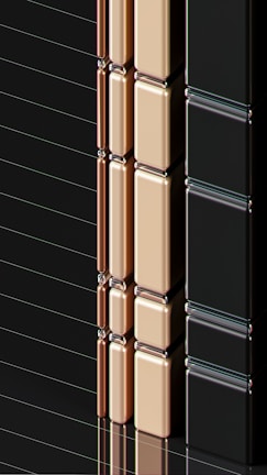 A series of glossy, rectangular tiles arranged vertically with a metallic finish. The tiles are colored in gold, copper, and black, creating a sleek and modern appearance. The surface reflects light, highlighting the smooth texture and polished edges.