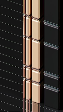 A series of glossy, rectangular tiles arranged vertically with a metallic finish. The tiles are colored in gold, copper, and black, creating a sleek and modern appearance. The surface reflects light, highlighting the smooth texture and polished edges.