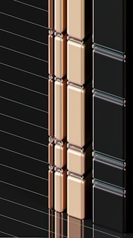 A series of glossy, rectangular tiles arranged vertically with a metallic finish. The tiles are colored in gold, copper, and black, creating a sleek and modern appearance. The surface reflects light, highlighting the smooth texture and polished edges.