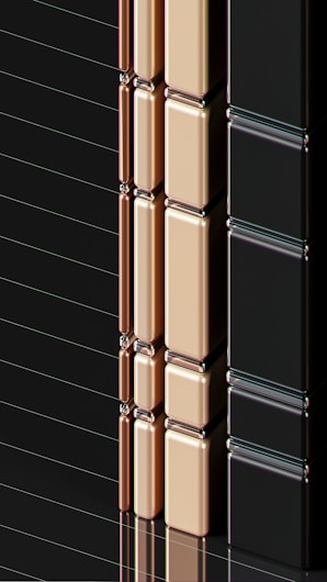A series of glossy, rectangular tiles arranged vertically with a metallic finish. The tiles are colored in gold, copper, and black, creating a sleek and modern appearance. The surface reflects light, highlighting the smooth texture and polished edges.