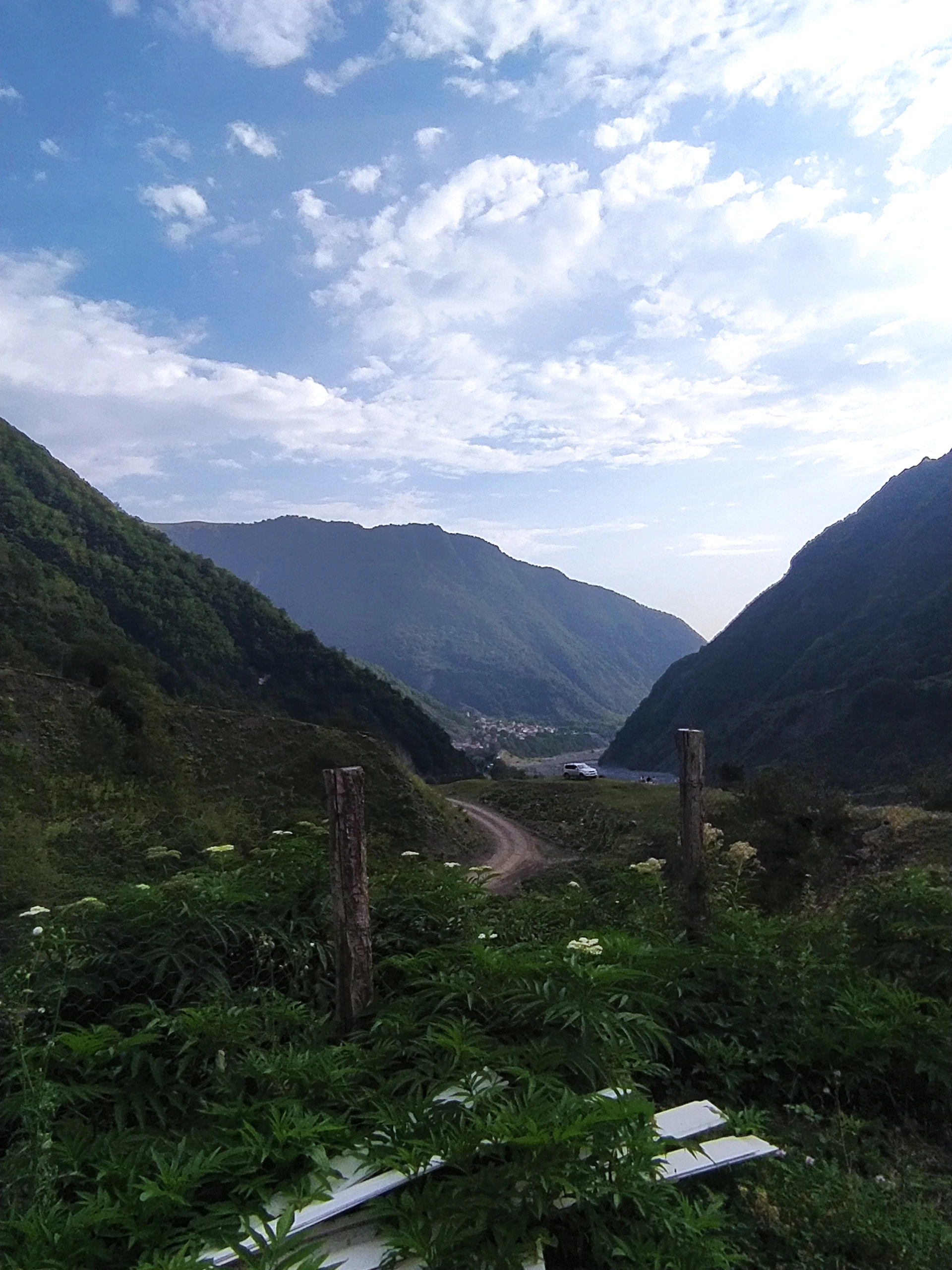 A panoramic shot of the Atlas Mountains with a Sellam Tours vehicle parked near a vibrant Berber village.
