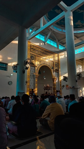 Congregation praying together inside Masjid Al Hujrah with sunlight filtering through stained glass