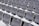 Rows of empty white plastic seats, each labeled with numbered tags, are neatly arranged in a stadium-like setting. The seats are aligned in perfectly straight rows on metal bleachers, creating a sense of order and uniformity.