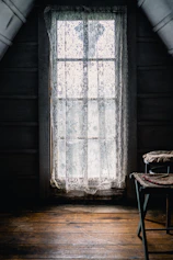 Cozy rustic pousada room with wooden beams and soft natural light filtering through lace curtains.