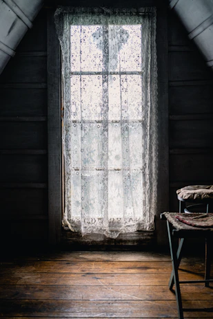 Cozy rustic pousada room with wooden beams and soft natural light filtering through lace curtains.