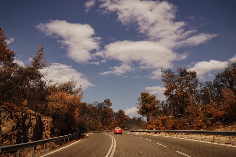 a red car driving down a road surrounded by trees