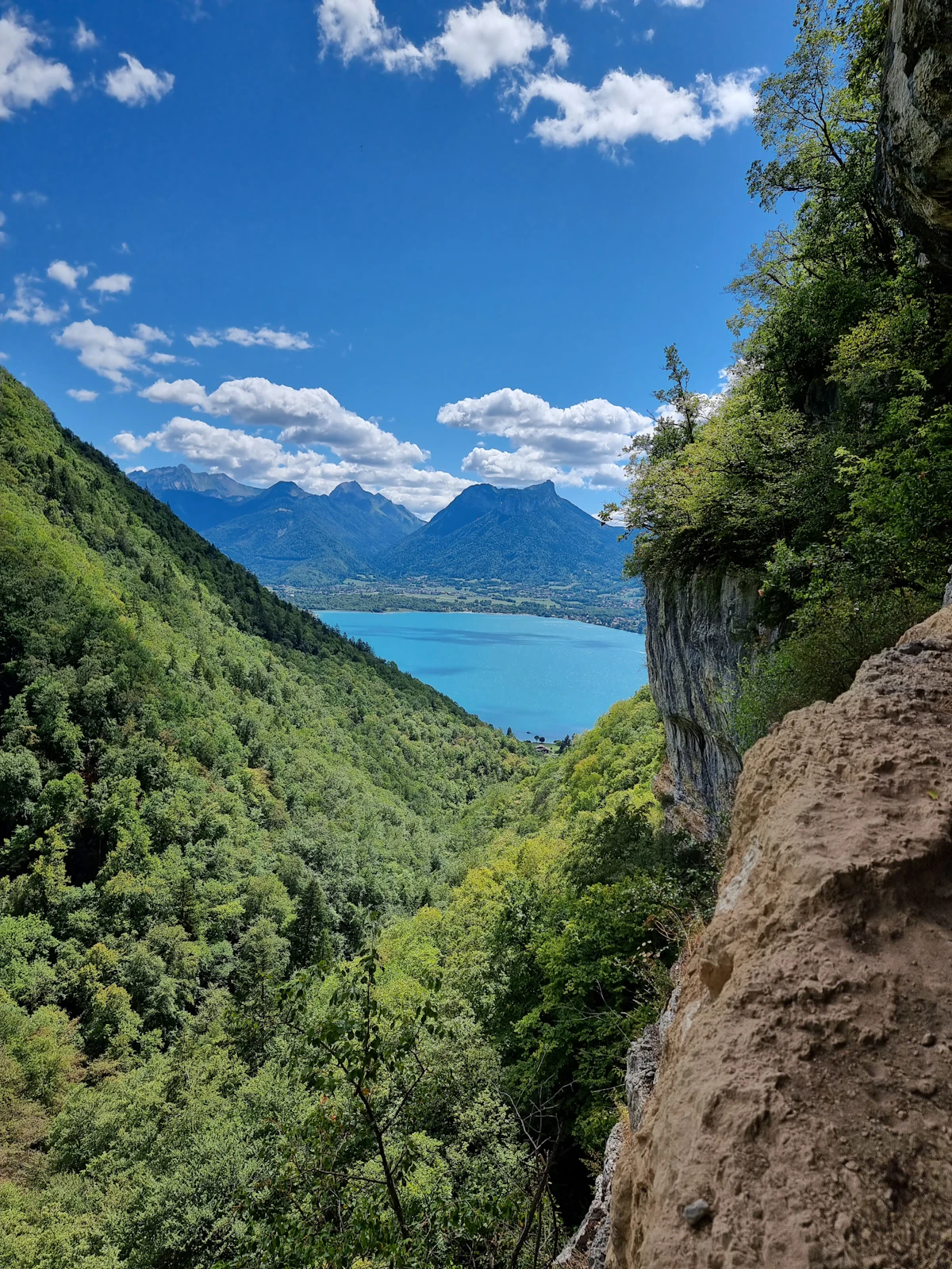 A wooded valley between cliffs opening onto Lake Annecy and the mountains beyond