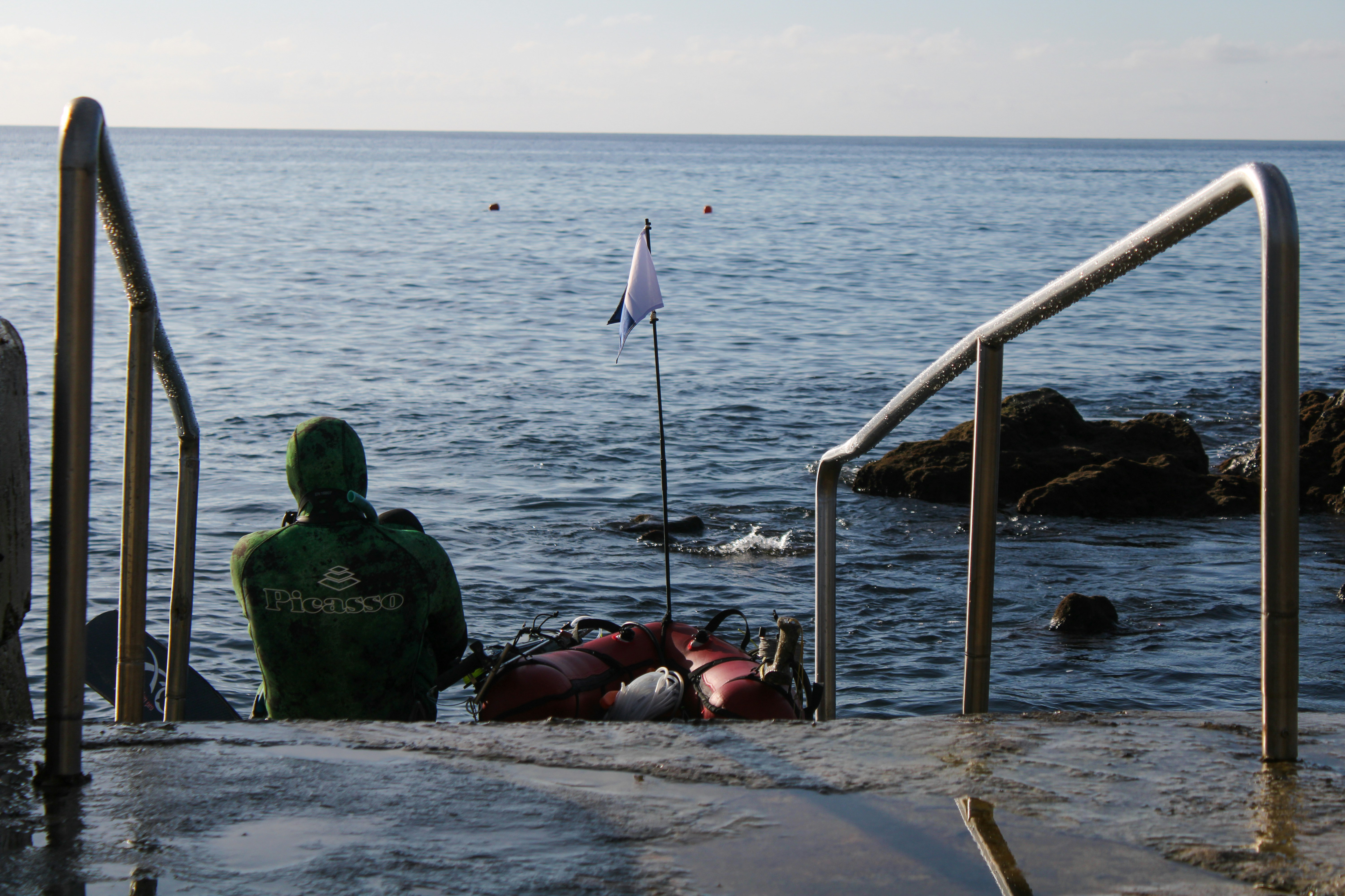 a man sitting on the edge of a pier next to the ocean