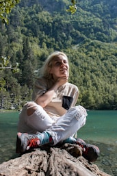 a woman sitting on top of a rock next to a lake