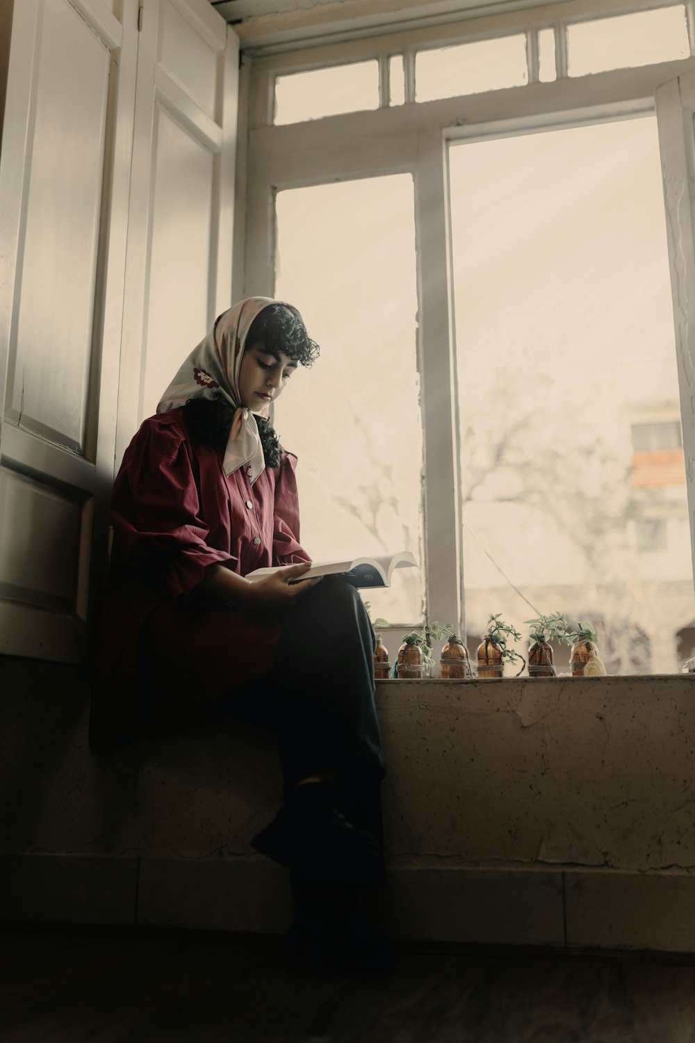 a woman sitting on a window sill reading a book