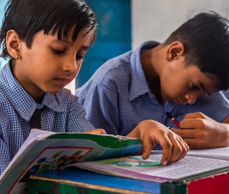 two young boys sitting at a desk with a book