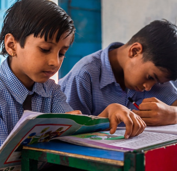 two young boys sitting at a desk with a book