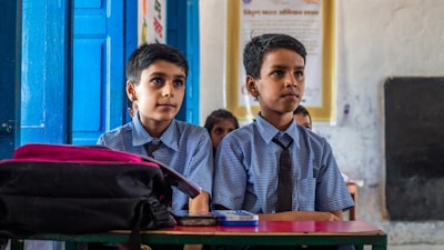 two young boys sitting at a desk in a classroom
