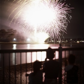 Families and friends enjoy the colorful fireworks reflection over the peaceful festival pond.