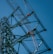 Several workers wearing safety gear are climbing a large metal lattice tower, which is possibly an electricity pylon. They use harnesses and ladders under a clear blue sky.