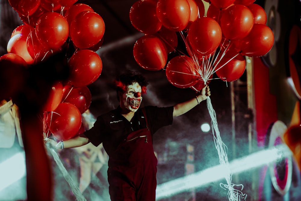 Un uomo in una maschera da clown che tiene palloncini rossi