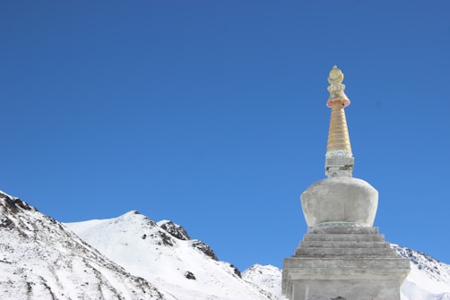 A Buddhist stupa with a golden spire set against a clear blue sky, surrounded by snow-covered mountains.