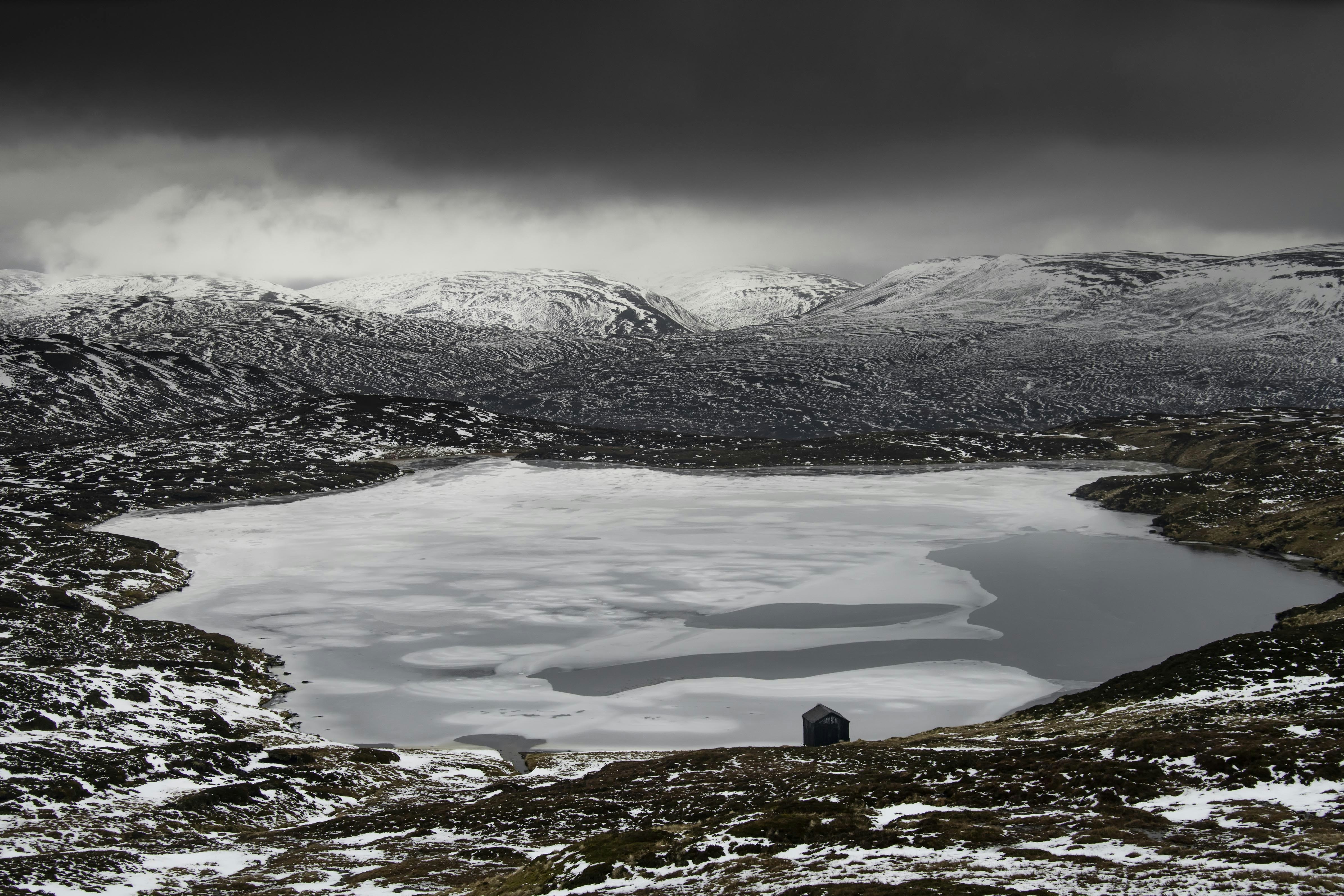 a lake surrounded by snow covered mountains under a cloudy sky