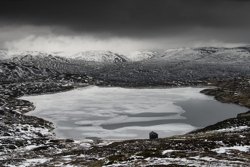 a lake surrounded by snow covered mountains under a cloudy sky