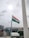 An Indian national flag is mounted on a pole, waving in the breeze against a cloudy sky. The background includes a cityscape with buildings and a few construction sites visible.