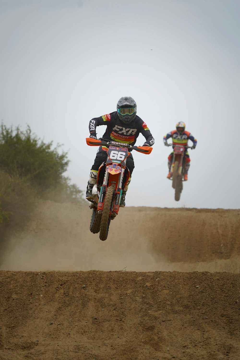 two motorcyclists are racing on a dirt track