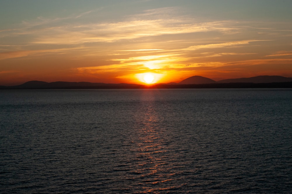 ein großes Gewässer mit einem Sonnenuntergang im Hintergrund