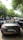 A convertible BMW Z4 with license plate WB02AP4224 is parked on a shaded street. Numerous people are gathered around various vehicles, under a canopy of lush green trees, suggesting a gathering or car meet.