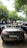 A convertible BMW Z4 with license plate WB02AP4224 is parked on a shaded street. Numerous people are gathered around various vehicles, under a canopy of lush green trees, suggesting a gathering or car meet.