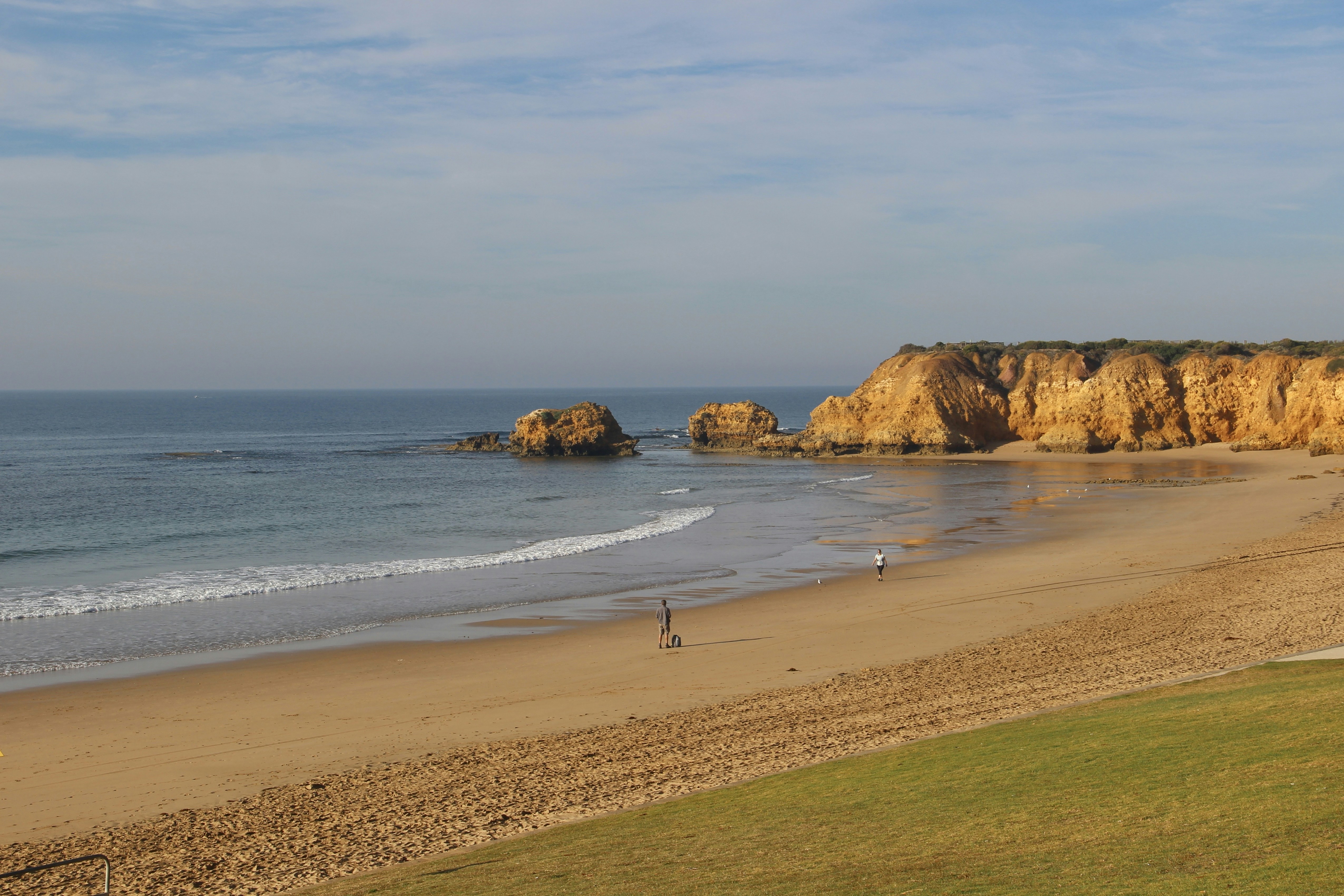 a sandy beach next to the ocean with a cliff in the background