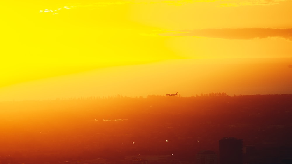 Die Sonne geht über einer Stadt mit einem Flugzeug in der Ferne unter