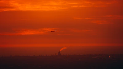 A vibrant sunset over the London skyline with an airplane silhouette.
