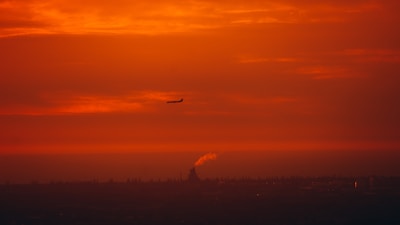 A vibrant sunset over a bustling city skyline with planes taking off in the distance.