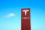A large red sign with the Tesla logo and brand name against a clear blue sky.