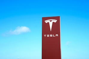 A large red sign with the Tesla logo and brand name against a clear blue sky.