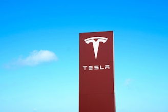 A large red sign with the Tesla logo and brand name against a clear blue sky.