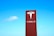 A large red sign with the Tesla logo and brand name against a clear blue sky.