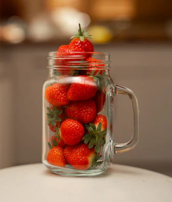 Hand pouring vibrant strawberry syrup into a glass jar surrounded by fresh strawberries