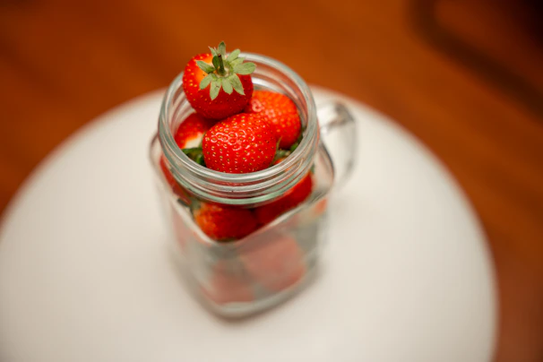 Bright red strawberry marmalade in a glass jar surrounded by fresh strawberries and green leaves