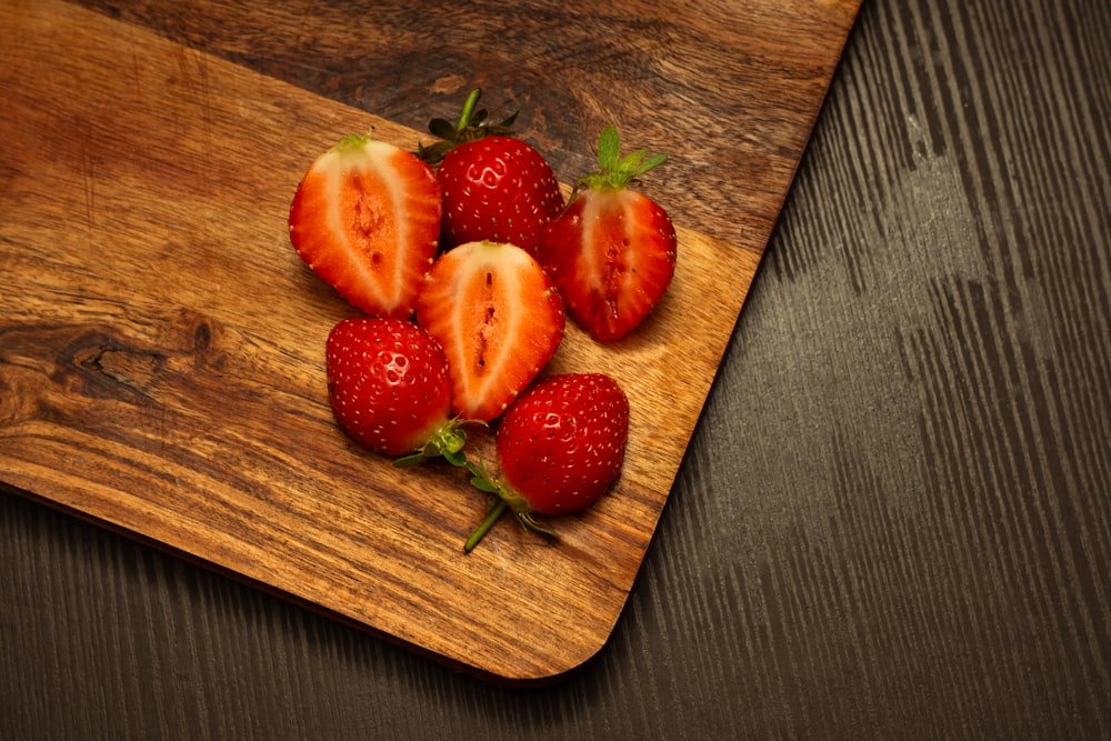 a wooden cutting board topped with strawberries on top of a table