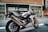 A sleek Honda motorcycle is parked on an urban street. The design of the motorcycle features a sporty build with a color scheme of white, red, and blue. It is positioned in front of a modern building with large windows and decorative patterns.